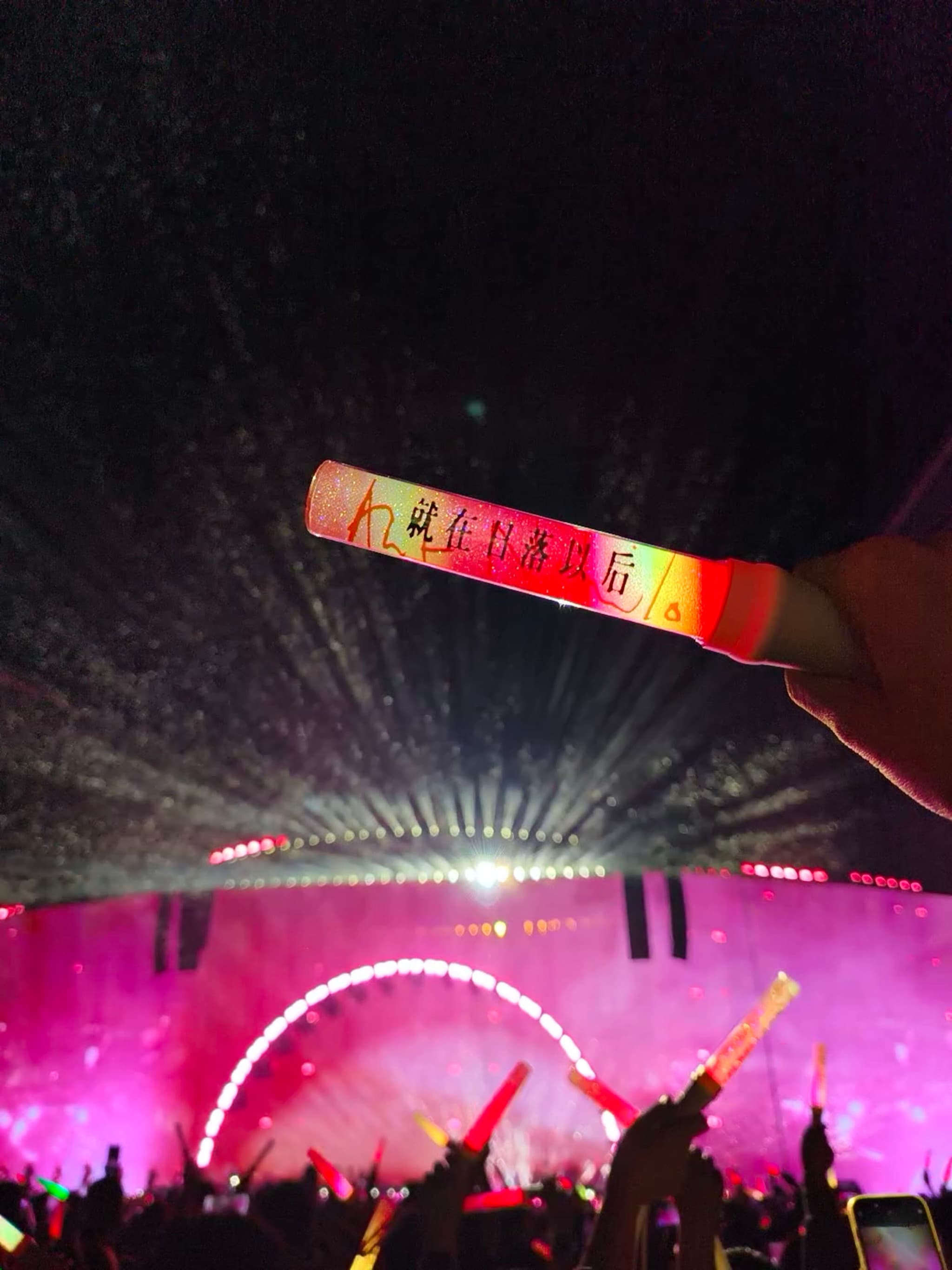 演唱会现场，一只手高举着发光的应援棒，下方是人群和灯光璀璨的舞台。