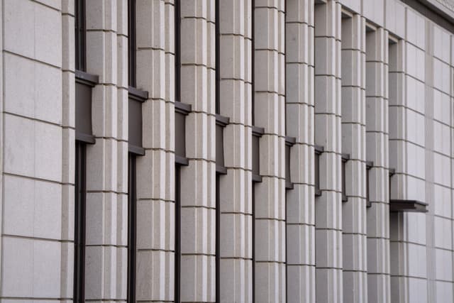 建筑外墙，由垂直的圆柱形结构和方形瓷砖组成，形成重复的图案。圆柱之间有窗户，整体呈现出几何和现代感。
