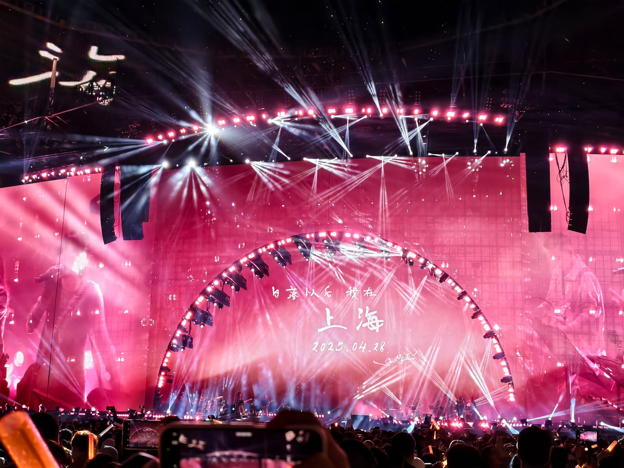 粉色灯光和激光束照亮了演唱会舞台，一个巨大的弧形灯光装置成为视觉焦点，台下可见观众。