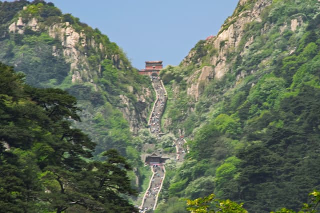 陡峭的石阶从山脚一直延伸到山顶，山顶有一座小建筑，周围是茂密的绿色植被。