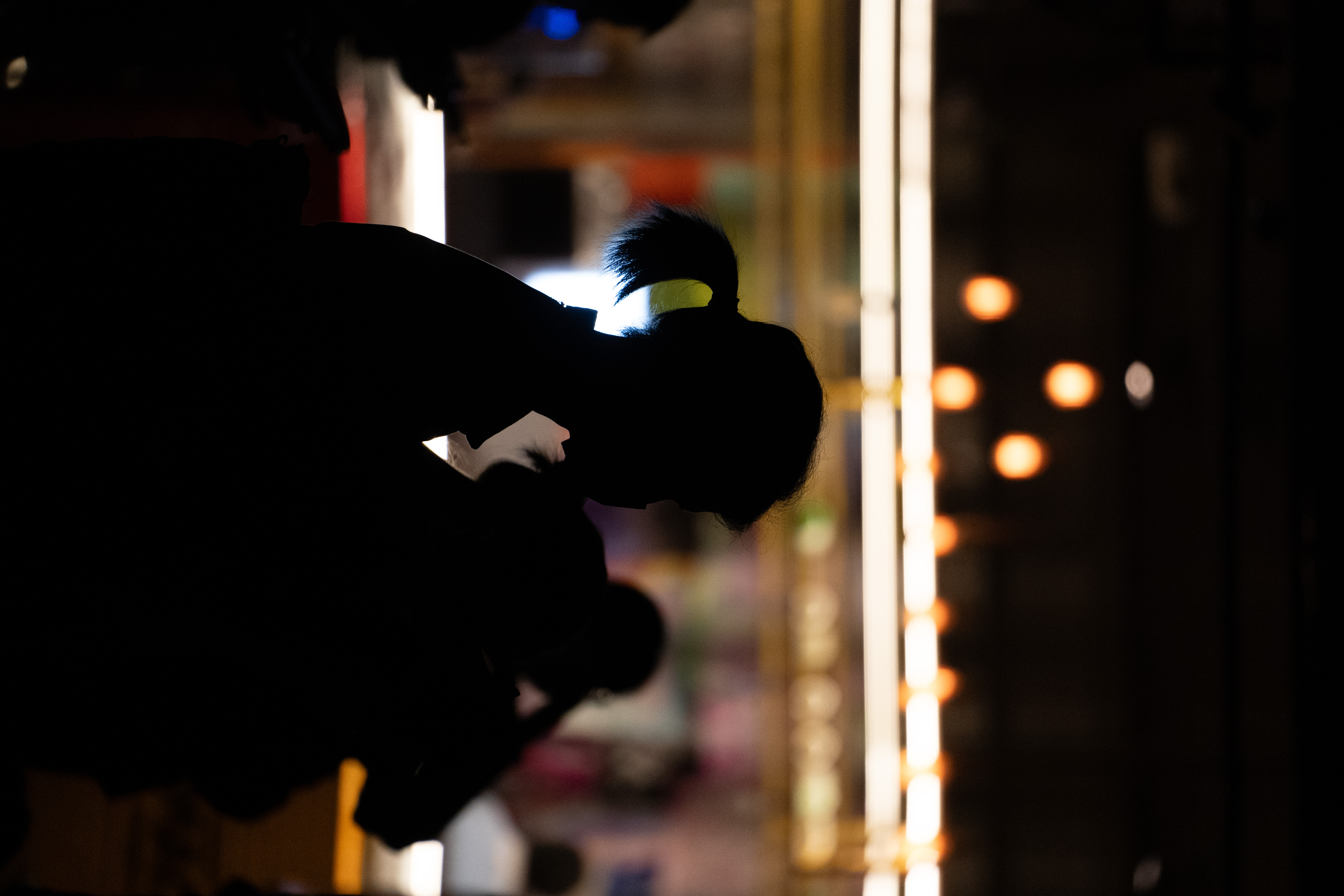 人物的剪影在昏暗的环境中显现，背景有模糊的灯光和室内装饰。